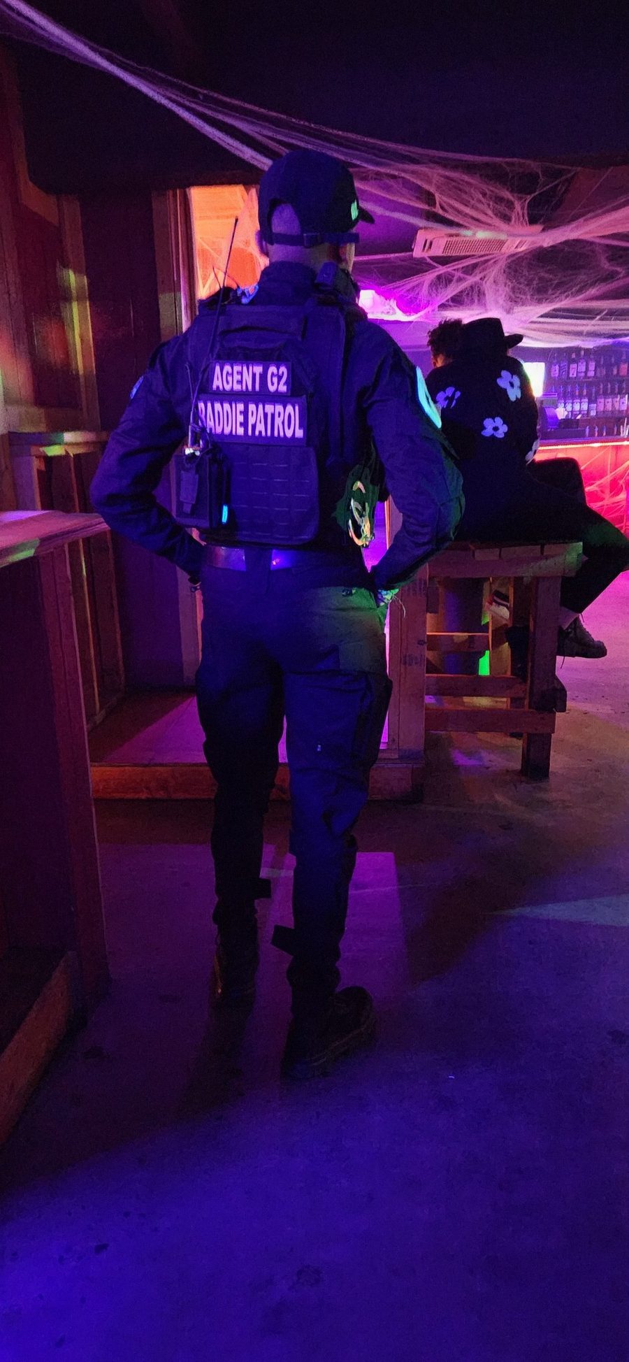 Back of Agent G2's tactical vest, patches reading Agent G2 and Baddie Patrol, under purple club lights
